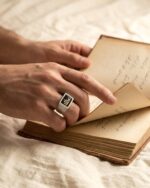 انگشتر شعر نقره با حکاکی روی دست کنار کتاب شعر باز