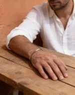 بنگل نقره لاین در دست مرد روی میز چوبی، فضا با دیوار کاهگل