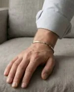 بنگل نقره مینیمال در دست مرد روی مبل پارچه‌ای